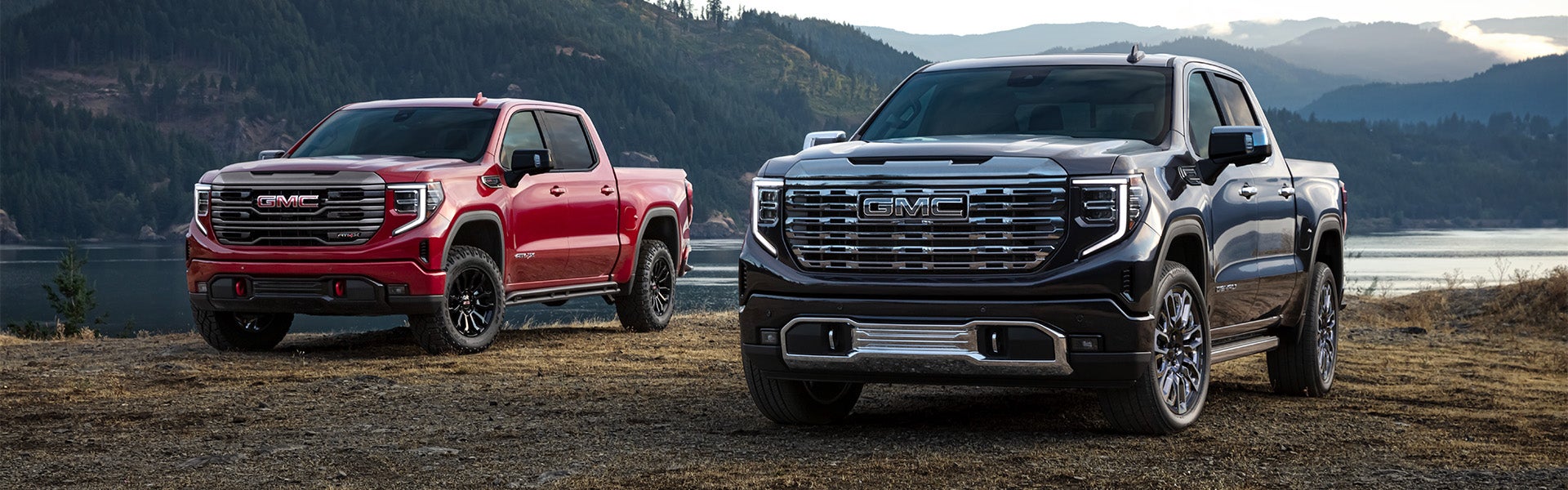 Two GMC Sierra 1500 trucks parked side by side with a mountain in the background