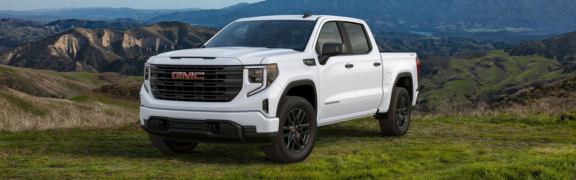 White GMC Sierra 1500 parked on the grass with a mountain in the background