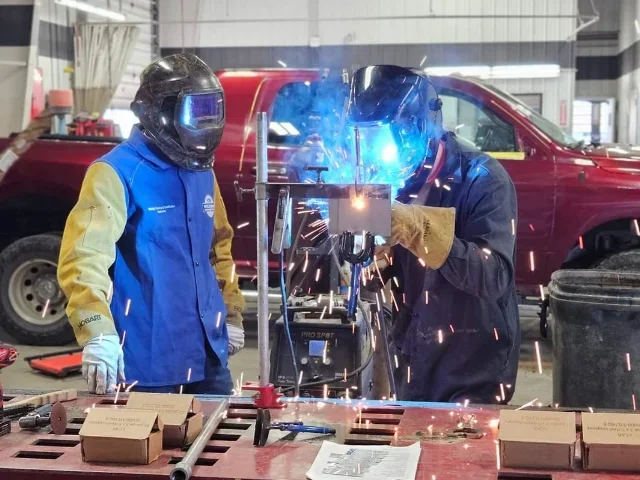 Two mechanics in a body shop using torch work on a car part