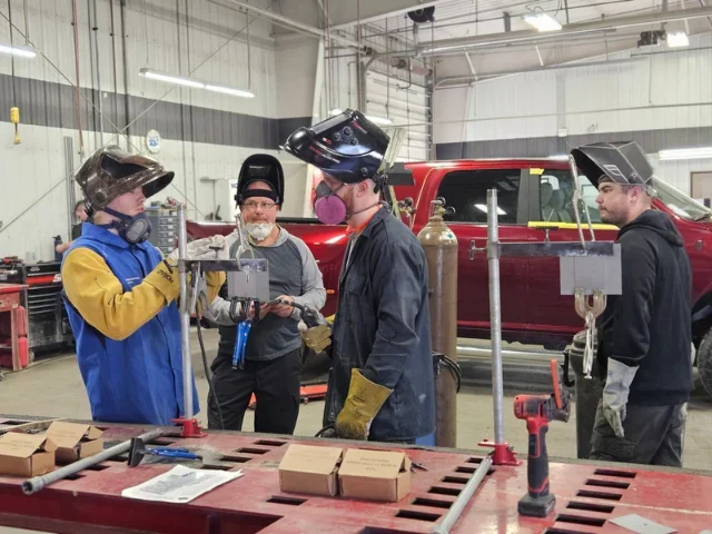 Four people standing in a warehouse planning work on a car